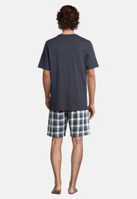 T-shirt blu navy a maniche corte, abbinato a pantaloni corti a quadri blu, bianchi e verdi. Vestibilità casual, tessuto morbido, visione posteriore.