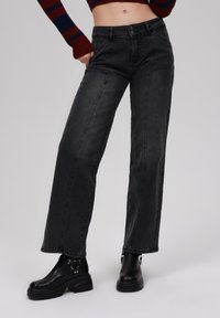 High-waisted, straight-leg black denim jeans with contrast stitching, front pockets, and a button closure. Paired with black platform boots.