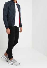 Marindjup lätt bomberjacka med röd foder, parat med en vit t-shirt och svarta slim-fit byxor, fullföljt med grå sneakers.