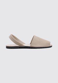 Sandalias de cuero beige tipo slingback con suela negra plana, que presentan un diseño minimalista y una caja de dedos ancha y angular.