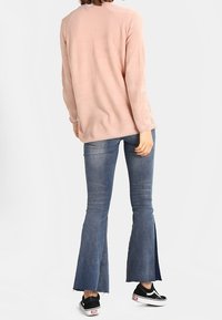 Maglione texturizzato rosa chiaro con maniche lunghe, abbinato a jeans a zampa d'elefante blu con orli spaccati e sneakers nere.