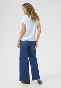 Un haut à rayures bleu clair à manches courtes associé à un jean large bleu foncé et des chaussures à enfiler marron, avec un design décontracté et relaxé.