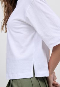 T-shirt bianco a maniche corte realizzato in cotone con taglio dritto, con spacchi laterali all'orlo, abbinato a una gonna verde plissettata.