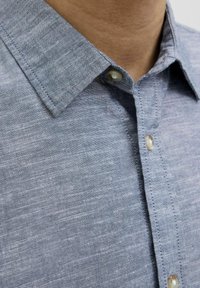 Cămașă cu nasturi, dintr-un material gri deschis cu un finisaj texturat, având un guler ascuțit și nasturi perle la nivelul placket-ului din față.