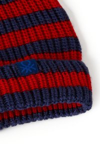 Pletená čepice s alternujícími červenými a námořnickými pruhy, s texturovaným vzorem a modrou etiketou zdobenou motivem sněhové vločky.