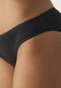 Svart bomullsbikini med en jämn textur, bred midja och inga synliga mönster eller detaljer. Skärningen ger full sidotäckning.