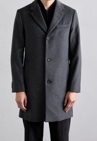Cappotto di lana grigio con design strutturato, monopetto, con rever a punto e quattro bottoni; presenta tasche laterali e vestibilità su misura.