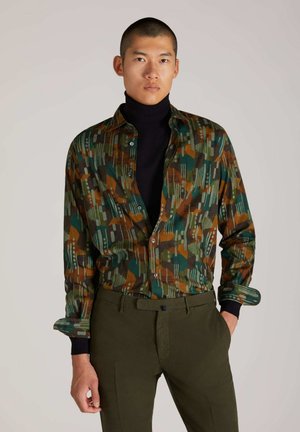 Camicia a maniche lunghe multi-color con motivi geometrici in verde, arancione e blu navy, abbinata a pantaloni verde oliva. Vestibilità casual e tessuto intrecciato.