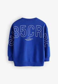 Blå sweatshirt med stor vit text på baksidan, med cirkulära designelement. Ribbad krage och ärmslut, mjukt texturerat tyg.