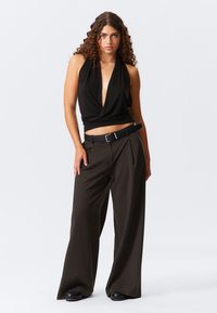 Top nero senza maniche con un design a profondo scollo a V e una vita aderente, abbinato a pantaloni larghi a vita alta di un verde oliva scuro e una cintura nera.