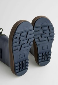 Bottes en caoutchouc avec semelles texturées bleu marine et accents marron. Présentent des motifs profonds pour une bonne adhérence et une zone de pointe renforcée. Design classique pour une durabilité accrue.