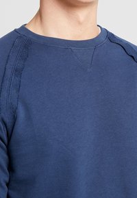 Blauwe katoenen sweatshirt met een ronde halslijn, ribgebreide boorden en een structuursteekdetail op de schouders. Zachte en gladde stofafwerking.
