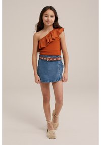 Top arancione a spalla unica con dettagli a volant, abbinato a una mini gonna di jeans blu, accentuato da una cintura floreale marrone e scarpe intrecciate beige.