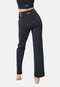 Zwarte sportbroek met een hoge tailleband, voorzien van subtiele gouden accenten en zijzakken, gemaakt van een soepele, rekbare stof.