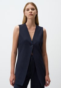 Gilet senza maniche blu navy con scollatura a V profonda, chiusura con un unico bottone, forma sagomata e tessuto liscio. Design semplice e moderno.