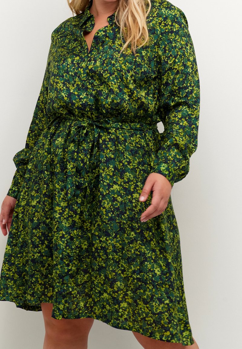 Robe fleurie verte à manches longues, boutonnée sur le devant, taille froncée, avec une ceinture à nouer. Tissu texturé avec un motif vibrant.