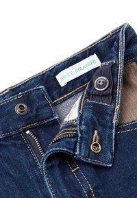 Jeans de mezclilla con un lavado azul oscuro. Presentan un cierre suave, herrajes de botón plateado y una etiqueta blanca con "BRUCE-STRAIGHT" en texto verde.