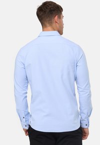 Lichtblauwe langarmsgemee shirt met een klassieke kraag, knoopmanchetten en een gladde textuur, met een gebogen zoom en stikseldetails.
