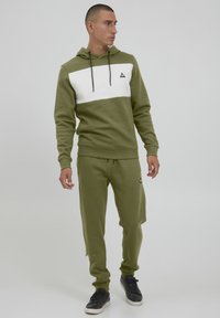 Olivgrüner Hoodie mit weißem Mittelteil, verstellbare Kapuze und Kordeln; kombiniert mit passenden Jogginghosen mit seitlichen Taschen und gerippten Bündchen.