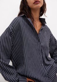 Chemise rayée bleu marine en tissu lisse, avec un front à boutons, un large col et des manches longues surdimensionnées avec une coupe décontractée.