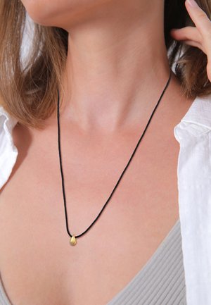 Schwarze Schnur-Halskette mit einem kleinen, goldenen Tropfenanhänger, getragen auf einem hellgrauen Oberteil, das minimalistisches Design und metallische Akzente hervorhebt.