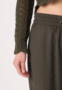 Olijfgroene, gebreide longsleeve top met een gestructureerd patroon; gecombineerd met losse olijfgroene broeken met een elastische tailleband.