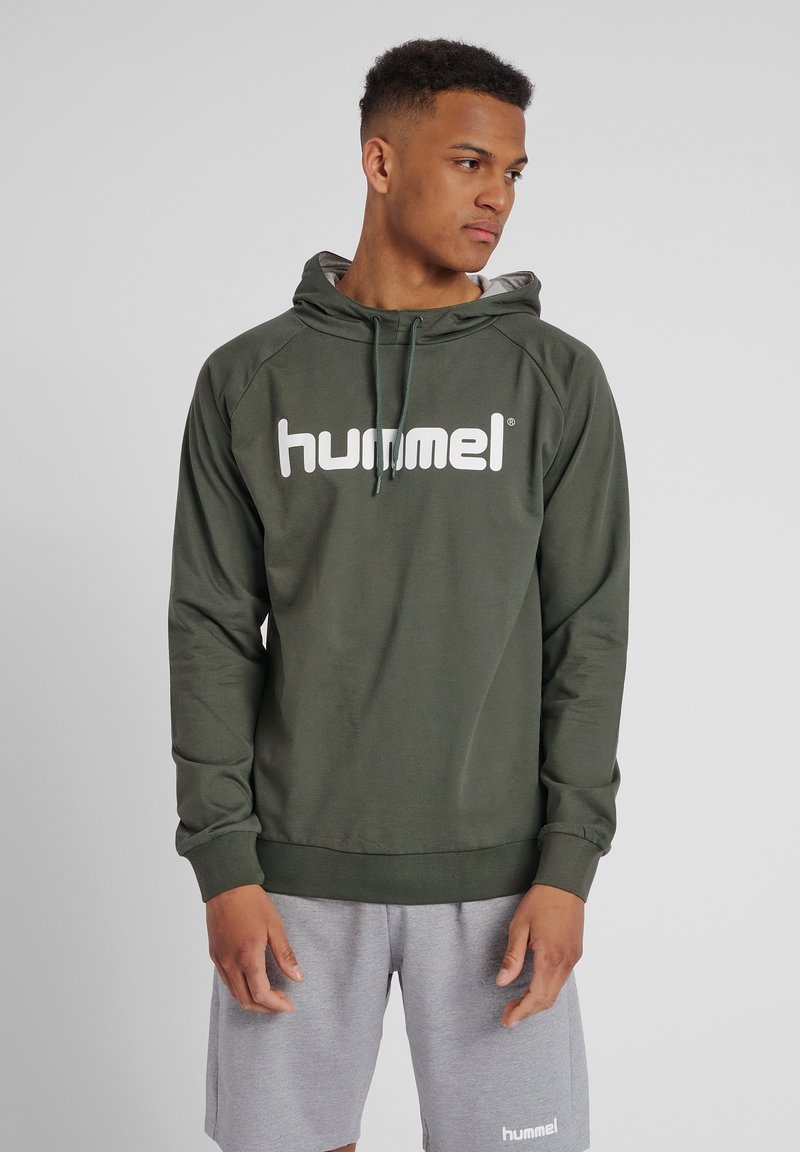 Hooded sweatshirt i olivgrön färg, tillverkad av mjukt material. Har en stor vit "hummel"-logotyp på framsidan, med kontrasterande dragsnören och ribbade ärmslut.