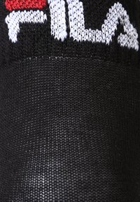 Μαύρη κάλτσα με λογότυπο Fila, που διαθέτει πλεκτό γράμμα σε κόκκινο και άσπρο χρώμα. Η υφή είναι λεία με σφιχτή ύφανση και ομοιόμορφο φινίρισμα.