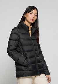 Giacca a vento nera con colletto alto, zip frontale e tasche laterali. Presenta un design trapuntato e una texture lucida.
