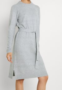Abito grigio a maglia con maniche lunghe, scollatura rotonda, vita cintrata e spacchi laterali all'orlo. Texture morbida e dettagli a costine sui polsini e sull'orlo.