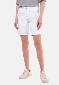 Shorts en denim blanc avec des poignets retroussés, dotés de poches avant et d'une fermeture éclair. Associés à des baskets claires et un haut rayé.
