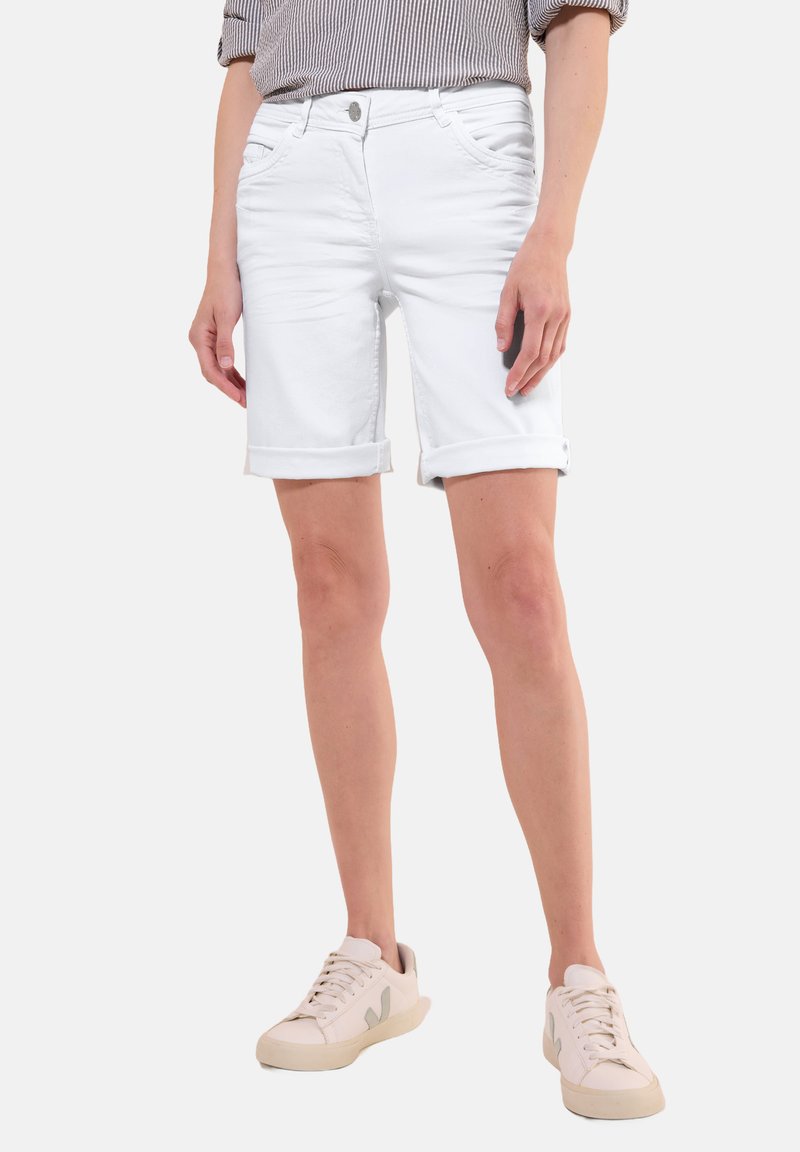 Shorts en denim blanc avec des poignets retroussés, dotés de poches avant et d'une fermeture éclair. Associés à des baskets claires et un haut rayé.