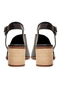 Paire de sandales à talons en cuir noir vues de dos, dotées de talons épais en bois superposés et de brides de cheville avec boucles argentées.