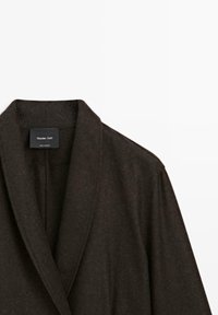 Dunkelbrauner Wollmantel mit Schalkragen und Etikett mit der Markenbezeichnung "Massimo Dutti". Die Textur wirkt weich und edel.