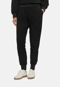 Pantaloni jogger neri realizzati in morbido cotone, con polsini elastici, tasche laterali e un discreto dettaglio testuale sulla gamba. Abbinati a sneakers bianche.