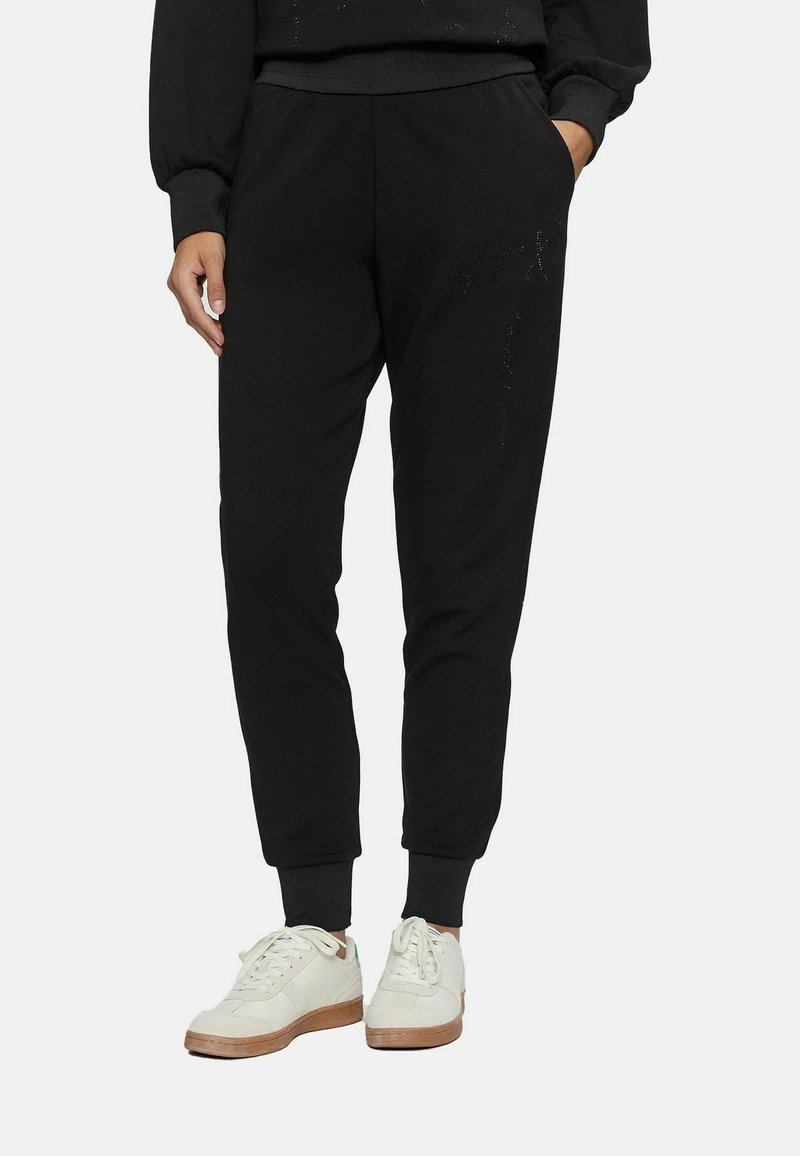 Pantaloni jogger neri realizzati in morbido cotone, con polsini elastici, tasche laterali e un discreto dettaglio testuale sulla gamba. Abbinati a sneakers bianche.