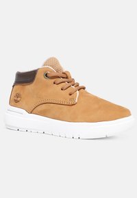 Baskets montantes en daim beige avec col marron, lacets ronds, semelle blanche épaisse et logo arbre sur le côté du talon.