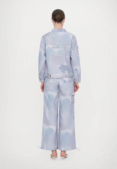 Lyseblå denimjakke og brede bukser med skydekor, med klaplommer og snore, glat tekstur og trykknapper.