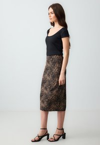 Zwarte geribbelde top met korte mouwen, gecombineerd met een middellange rok met luipaardprint. De rok heeft afwisselende bruin- en zwarttinten. Zwarte sandaaltjes met banden.