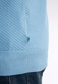 Světle modrý svetr s texturovaným diagonálním vzorem, ribbeným lemem a malým logem na boku. Materiál vypadá jemně a pleteně.