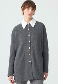 Šedý žebrovaný cardigan s bílým límcem, se zlatými knoflíky vpředu, dlouhými rukávy a uvolněným střihem. Hladká textura.