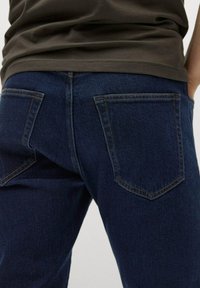 Jeans de denim azul oscuro con una textura suave, que cuentan con dos bolsillos traseros y costuras en naranja contrastante a lo largo de las costuras.