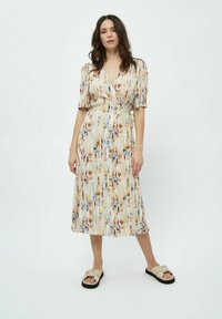 Blumen-Wickelkleid mit kurzen Puffärmel, knielanger Rock in cremefarbenen, orangefarbenen, blauen und braunen Mustern; kombiniert mit beigen Sandalen.