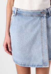 Mini-jupe en denim bleu clair avec ourlet brut, dotée de passants de ceinture, d'une fermeture à bouton sur le devant et de coutures contrastées. Texture lisse.