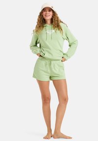 Sudadera de algodón verde claro con bolsillo frontal y cordón, combinada con pantalones cortos a juego que cuentan con una cintura elástica.