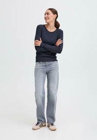 Maglione lavorato a maglia navy con un motivo testurizzato, abbinato a jeans dritti grigio chiaro e sneakers beige con strisce nere.