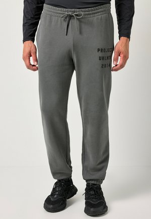 La persona indossa pantaloni della tuta grigi con vita elastica e testo nero "PROJECT UNLMTD 2014" sulla coscia sinistra, abbinati a scarpe sportive nere.