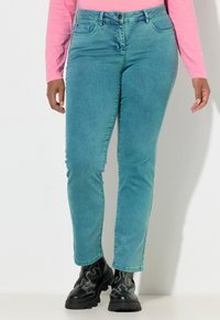 Turkusowe dżinsy z denimu o wąskim kroju, z pięcioma kieszeniami i talią o średnim stanie. Noszone z czarnymi, masywnymi butami. Tkanina o fakturze i gładkim wykończeniu.