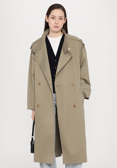 Khaki trench coat with a double-breasted design, shoulder epaulets, and wooden buttons, paired with a black cardigan and light jeans.