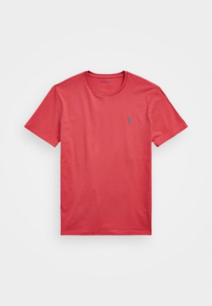 T-shirt en coton rouge avec un col rond, des manches courtes et un petit logo bleu sur la poitrine gauche. Texture lisse, design décontracté.